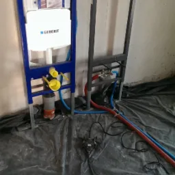 Stelaże podtynkowe WC Geberit Sigma w trakcie montażu, widoczne rury doprowadzające wodę i odpływ, zabezpieczone folią podłoże.