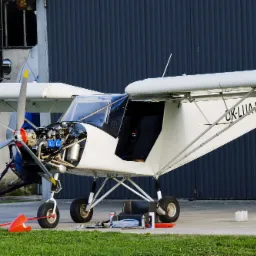 Biały samolot ultralekki z otwartą maską silnika, narzędzia i części widoczne na ziemi, czerwony statecznik pionowy, numer rejestracyjny OK-LUA-37.