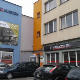Fasada budynku z szyldami firm Marion, Mail Boxes Etc. i Prawko, z zaparkowanymi samochodami na pierwszym planie.
