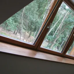 Drewniane okno dachowe z widokiem na las, częściowo otwarte, z drewnianym parapetem.