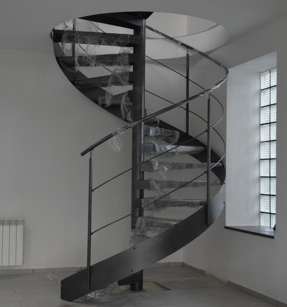 Metalowe schody spiralne z tymczasowym zabezpieczeniem folią, widoczne okno z luksferami i grzejnik w minimalistycznym wnętrzu.