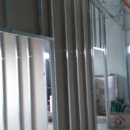 Konstrukcja ścian działowych z profili metalowych i płyt gipsowo-kartonowych w trakcie montażu, widoczne przewody instalacyjne pod sufitem.