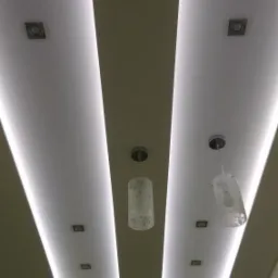 Sufit z podwieszanymi pasami i oświetleniem LED, dwa wiszące klosze z delikatnym wzorem, symetryczny układ punktowych lamp.