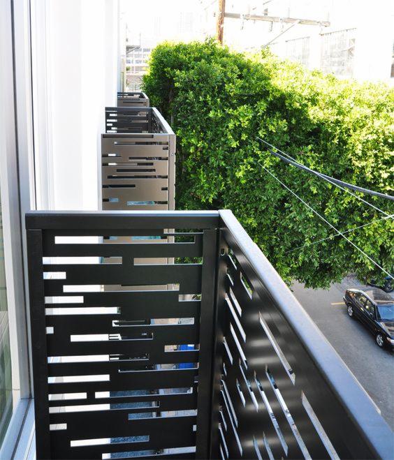 Nowoczesna zabudowa balkonu z czarnych, metalowych paneli z poziomymi wycięciami, widok z góry na ulicę i zieleń