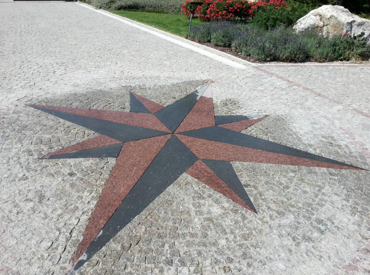 Kompozycja w kształcie gwiazdy, ułożona z czerwono-czarnych elementów na jasnoszarej kostce brukowej, tworząca dekoracyjny wzór na posesji prywatnej.
