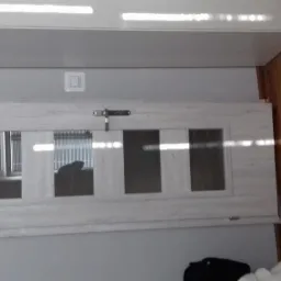 Zamontowane okno z trzema szybami w jasnej ramie, widoczne z poziomu podłogi, z odbiciem żaluzji w szybach.