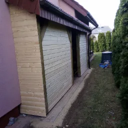 Drewniana zabudowa tarasu przylegająca do ściany domu, widoczna z boku, z otwartym wejściem i elementami konstrukcyjnymi z belek drewnianych.