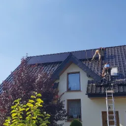 Montaż paneli słonecznych na dachu domu w Gdańsku przez dwóch pracowników, widoczna drabina oparta o dach i okno dachowe.