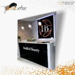 Nowoczesna recepcja w gabinecie Health & Beauty z czarnym, błyszczącym frontem i logo HB, oświetlona wiszącymi lampami.