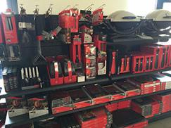 Ekspozycja akcesoriów do grillowania na czarnym regale w sklepie, widoczne czerwone opakowania i srebrne narzędzia.