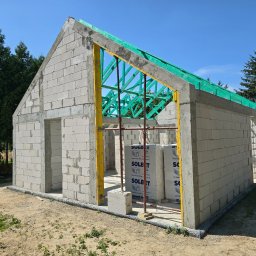 Firma Remontowo Budowlana HOP- home our passion - Niedokończony budynek z betonu komórkowego z widocznym szalunkiem i zieloną konstrukcją dachu, na zewnątrz leżą bloczki Solbet