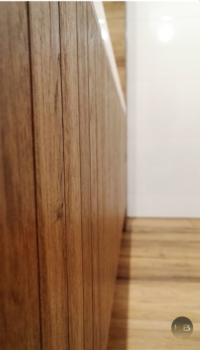 Detal drewnianej obudowy wanny z widoczną podłogą z paneli w łazience z białymi płytkami.