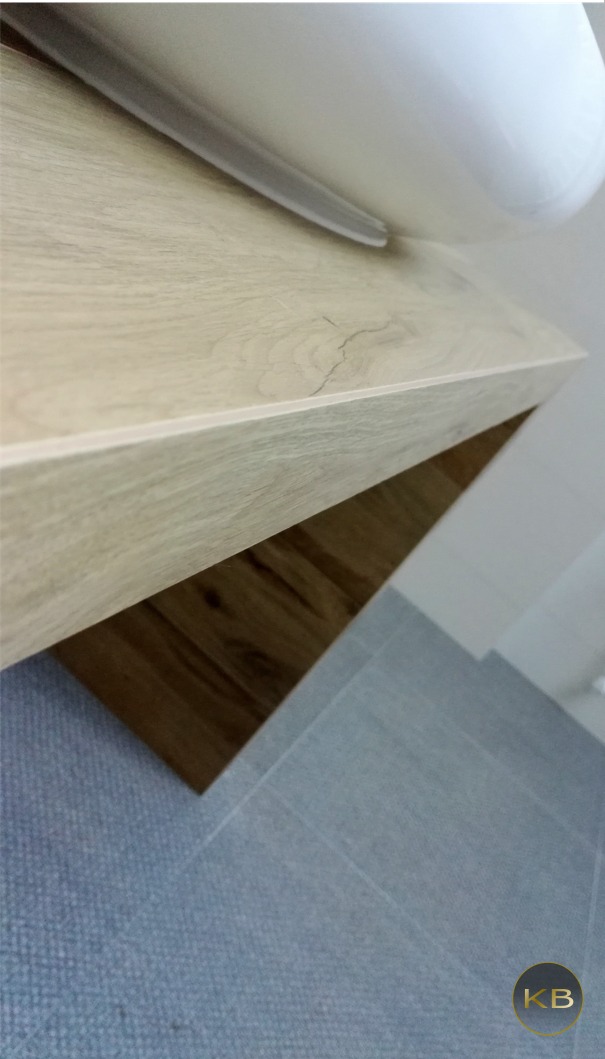 Fragment łazienki z umywalką nablatową, blatem z jasnego drewna i szarymi płytkami podłogowymi, widoczne łączenie blatu z umywalką.