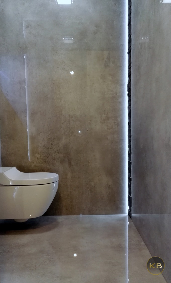 Nowoczesna toaleta podwieszana w łazience wykończonej płytami w odcieniach szarości z subtelnym oświetleniem LED w szczelinie między płytami.