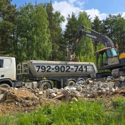 Wyburzenia Pomorze sp.zoo - Żółto-szara koparka Volvo ładuje gruz do ciężarówki z numerem telefonu na tle zieleni. Widok na etap prac ziemnych lub wywóz gruzu po rozbiórce.