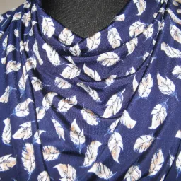 Fragment drapowanej, granatowej tkaniny z wzorem piór w odcieniach bieli i beżu, ułożonej na manekinie krawieckim.