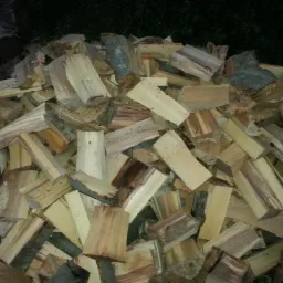 Stos pociętego drewna kominkowego z widocznymi słojami, ułożony na ziemi w słabym oświetleniu.