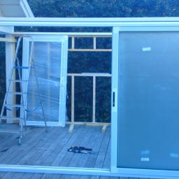 KONCEPT Justyna Łuczak - Montaż przeszklonej konstrukcji tarasowej z przesuwnymi drzwiami, widoczna drabina, narzędzia i częściowo zdemontowana ściana.