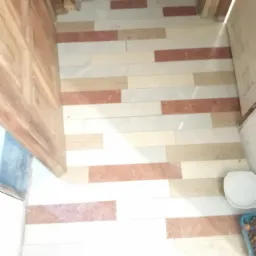 Ułożone płytki podłogowe w łazience w odcieniach bieli, beżu i terakoty, z widocznym fragmentem drzwi i miską.