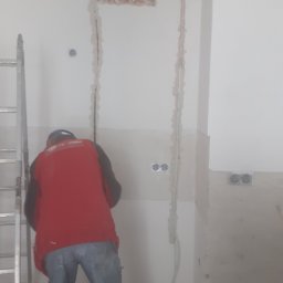 Henryk  Borysowicz - Instalacja elektryczna w bruzdach ściennych podczas prac wykończeniowych, widoczna drabina i fragment sylwetki pracownika w czerwonej koszulce.