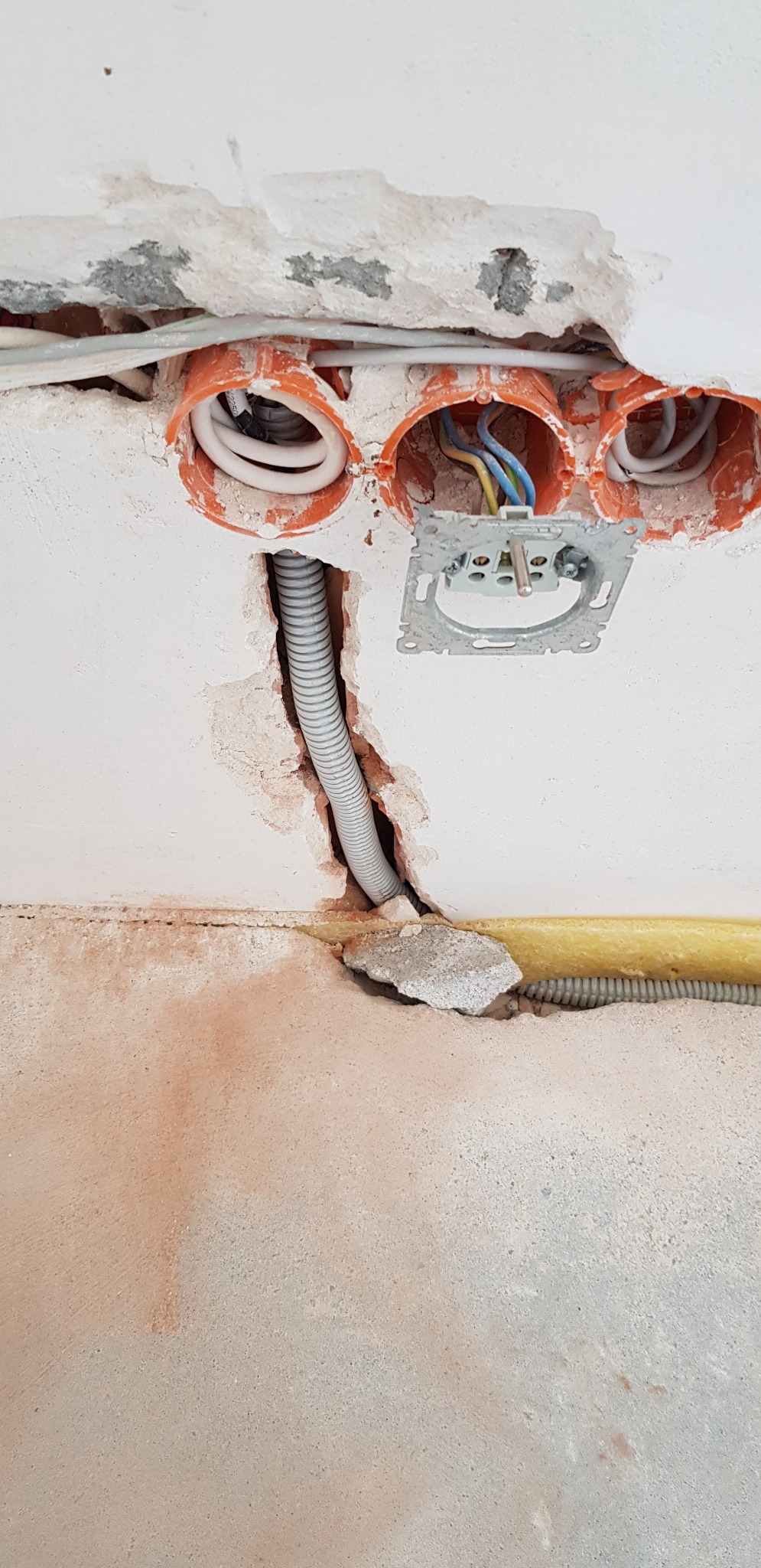 Przygotowanie instalacji elektrycznej w ścianie: puszki instalacyjne, przewody w peszlu, uchwyt gniazdka, surowy tynk z ubytkami.