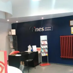 Wnętrze placówki finansowej Fines z biurkiem obsługi klienta, regałem z ulotkami i plakatem reklamowym z hasłem 'Tutaj otrzymasz kredyt!'