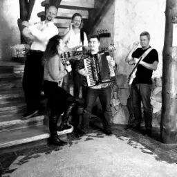Czarno-białe zdjęcie zespołu muzycznego grającego na schodach, w składzie akordeonista, gitarzysta, basista, perkusista i wokalistka w wysokich butach.