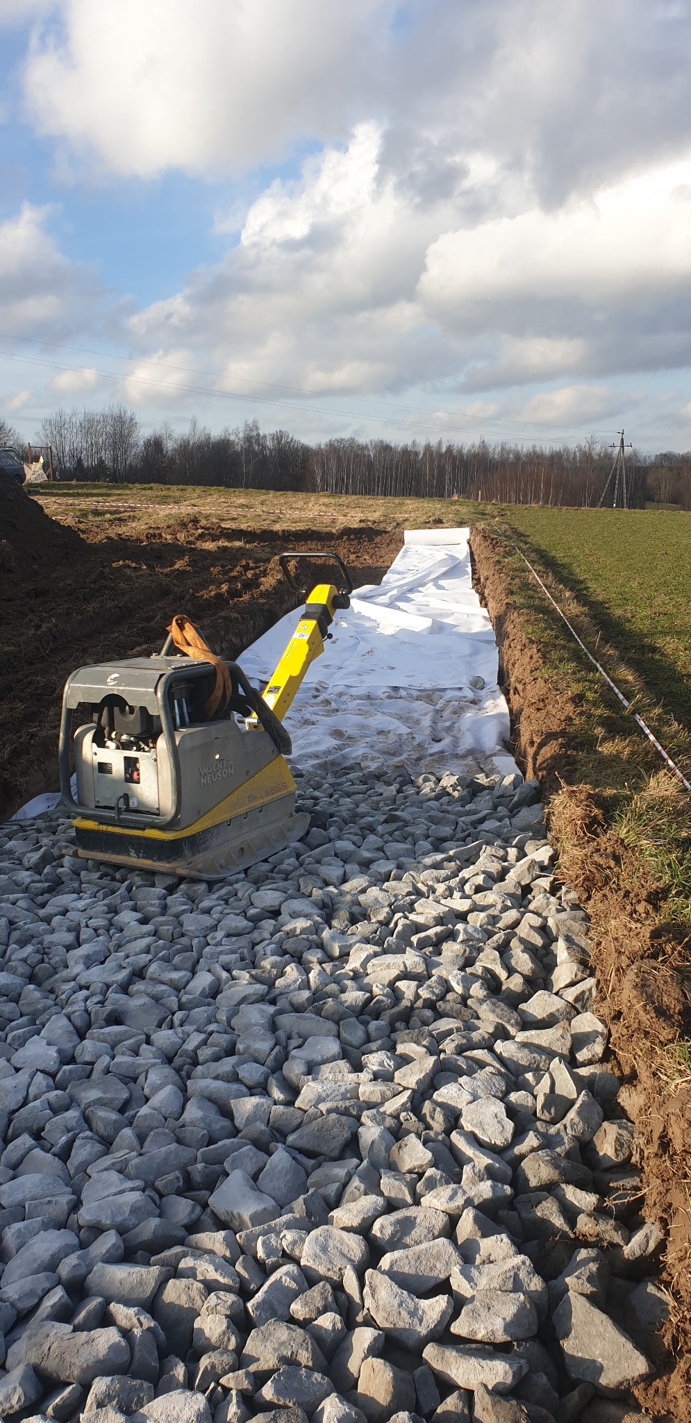 Wacker Neuson ubijak stopowy na podsypce z kamienia w wykopie zabezpieczonym geowłókniną, przygotowanie pod utwardzenie drogi.