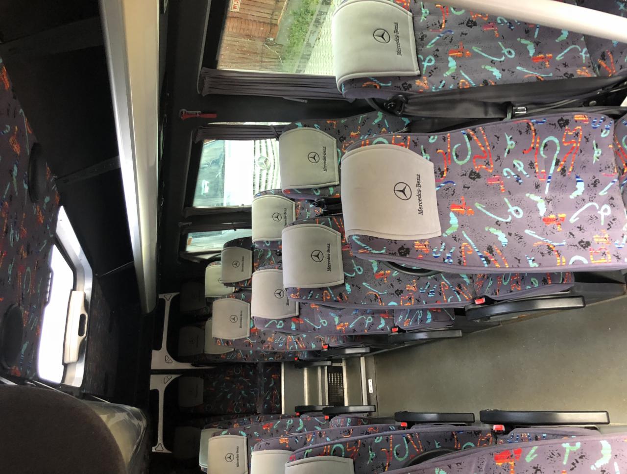 Wnętrze autobusu z rzędami foteli z zagłówkami marki Mercedes-Benz, widoczne z perspektywy pasażera.