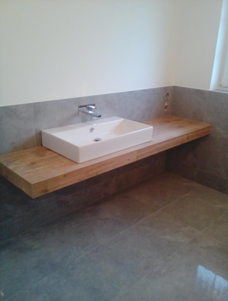 Nowoczesna łazienka z prostokątną białą umywalką nablatową na drewnianym blacie, szare płytki na ścianie i podłodze, minimalistyczna bateria.