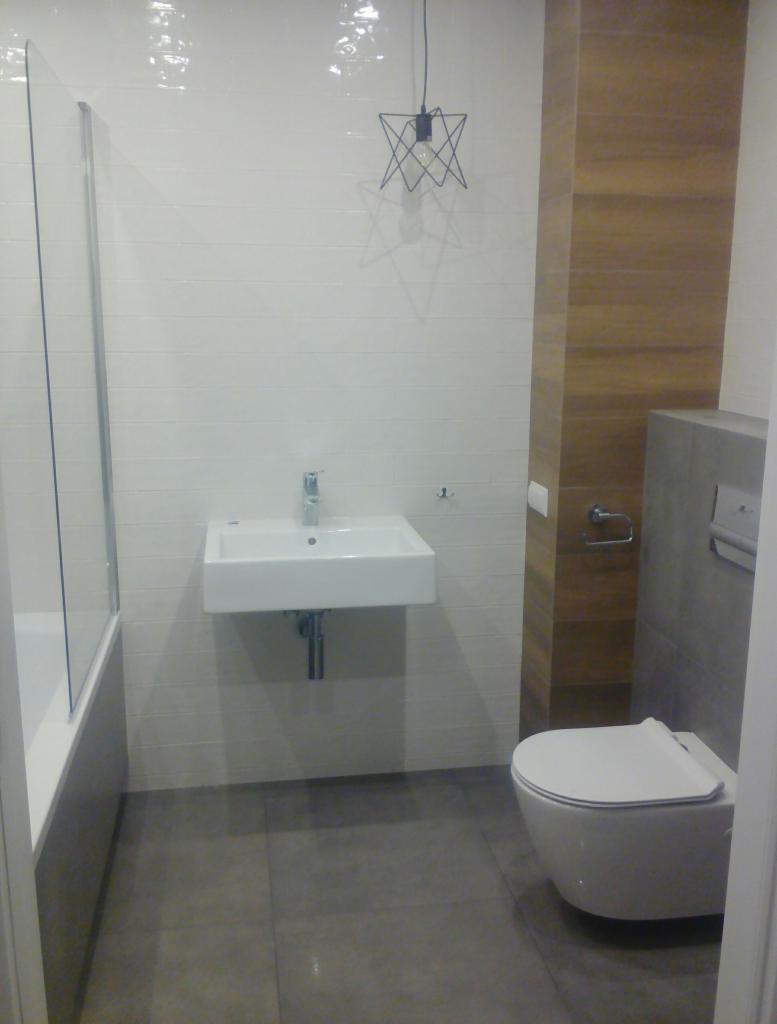 Nowoczesna łazienka z białymi płytkami, wiszącą umywalką, podwieszaną toaletą i ozdobną lampą sufitową w kształcie gwiazdy.