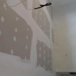 Ściana po montażu płyt kartonowo-gipsowych, z widocznymi łączeniami wzmocnionymi taśmą i miejscami po wkrętach, przygotowana do dalszych prac wykończeniowych, takich jak szpachlowanie.