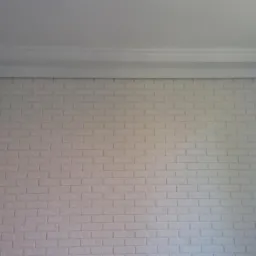 Ściana z białej cegły z widoczną sztukaterią sufitową, szary narożnik ściany z przewodem.