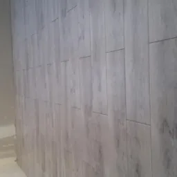 Ściana wyłożona panelami imitującymi drewno w trakcie prac wykończeniowych, widoczne ślady po zaprawie na sąsiedniej ścianie.