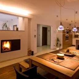 Nowoczesne wnętrze domu z otwartą przestrzenią: salon z kominkiem oddzielony od jadalni i kuchni, drewniane podłogi i meble, oświetlenie punktowe i wiszące lampy.