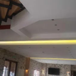 Wielopoziomowy sufit z oświetleniem LED w nowoczesnym wnętrzu z ceglanymi ścianami i spiralnymi schodami.