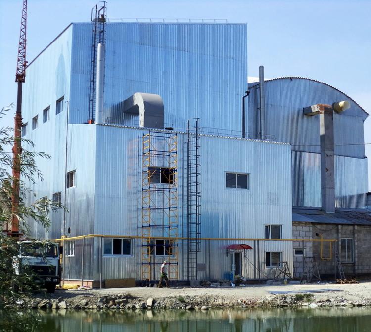 Zewnętrzny widok gotowej hali stalowej z blachy falistej, z widocznymi schodami, rusztowaniami i fragmentem ciężarówki na pierwszym planie, odbijającej się w wodzie.