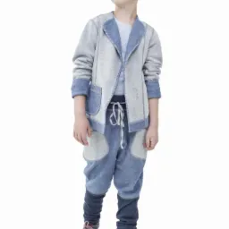 Chłopiec w szarym blezerze z niebieskimi wykończeniami i dresowych spodniach z naszytymi łatami, pozujący na białym tle.