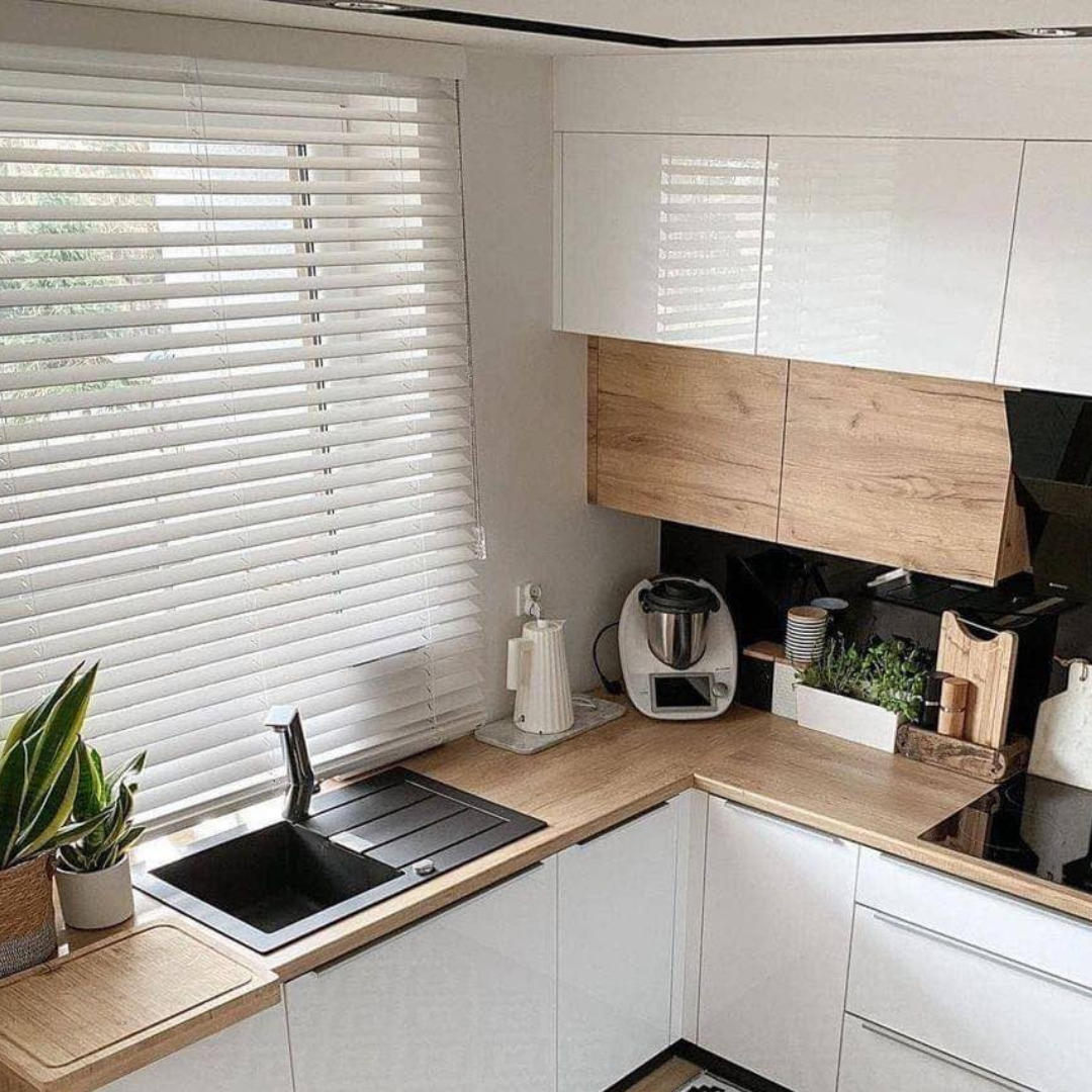 Białe, poziome żaluzje w nowoczesnej kuchni z białymi szafkami i drewnianym blatem.