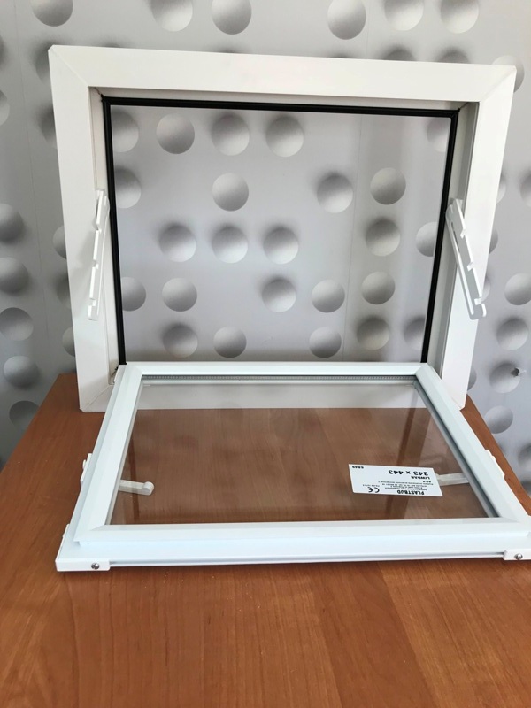 Biała rama okienna z uchylnym mechanizmem, widoczna etykieta producenta na szybie, tło w geometryczne wzory.