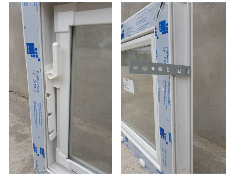 Fragment montażu białego okna PCV z widoczną klamką i metalowym wspornikiem mocującym, folia ochronna częściowo zdjęta.