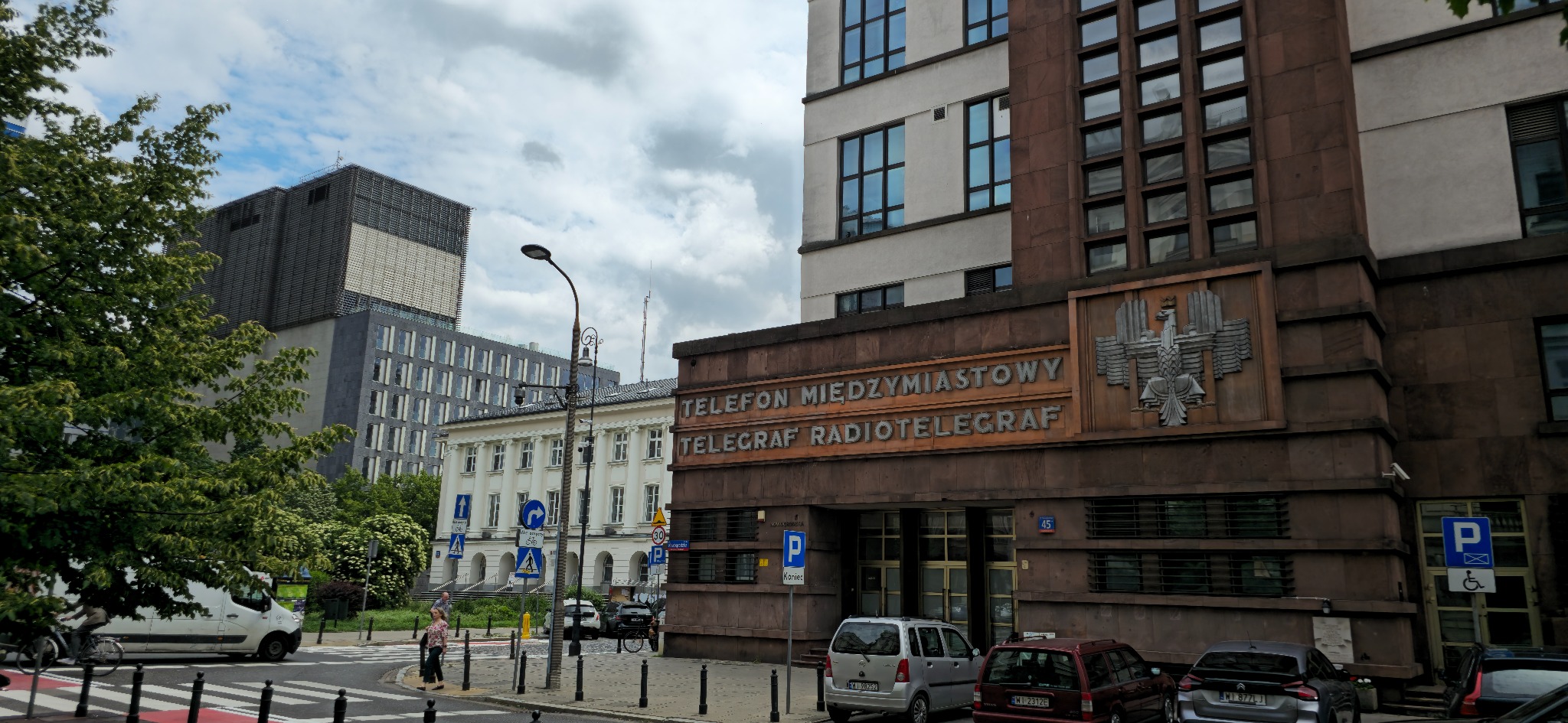 Fasada budynku z napisem 'Telefon Międzymiastowy Telegraf Radiotelegraf' i godłem Polski, widok z ulicy w słoneczny dzień.