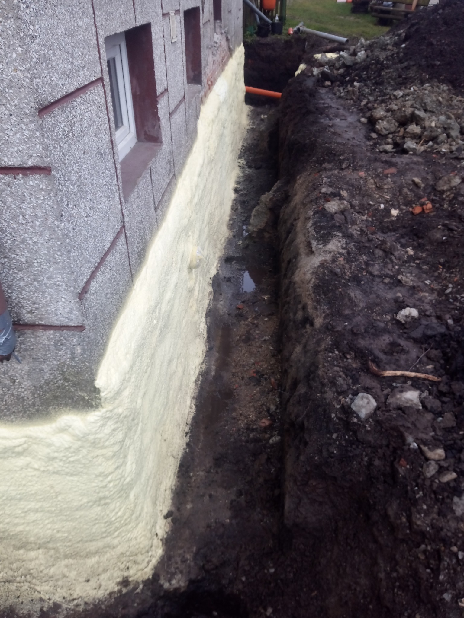 Izolacja fundamentów budynku mieszkalnego za pomocą piany poliuretanowej, widoczny wykop i odsłonięte fundamenty.