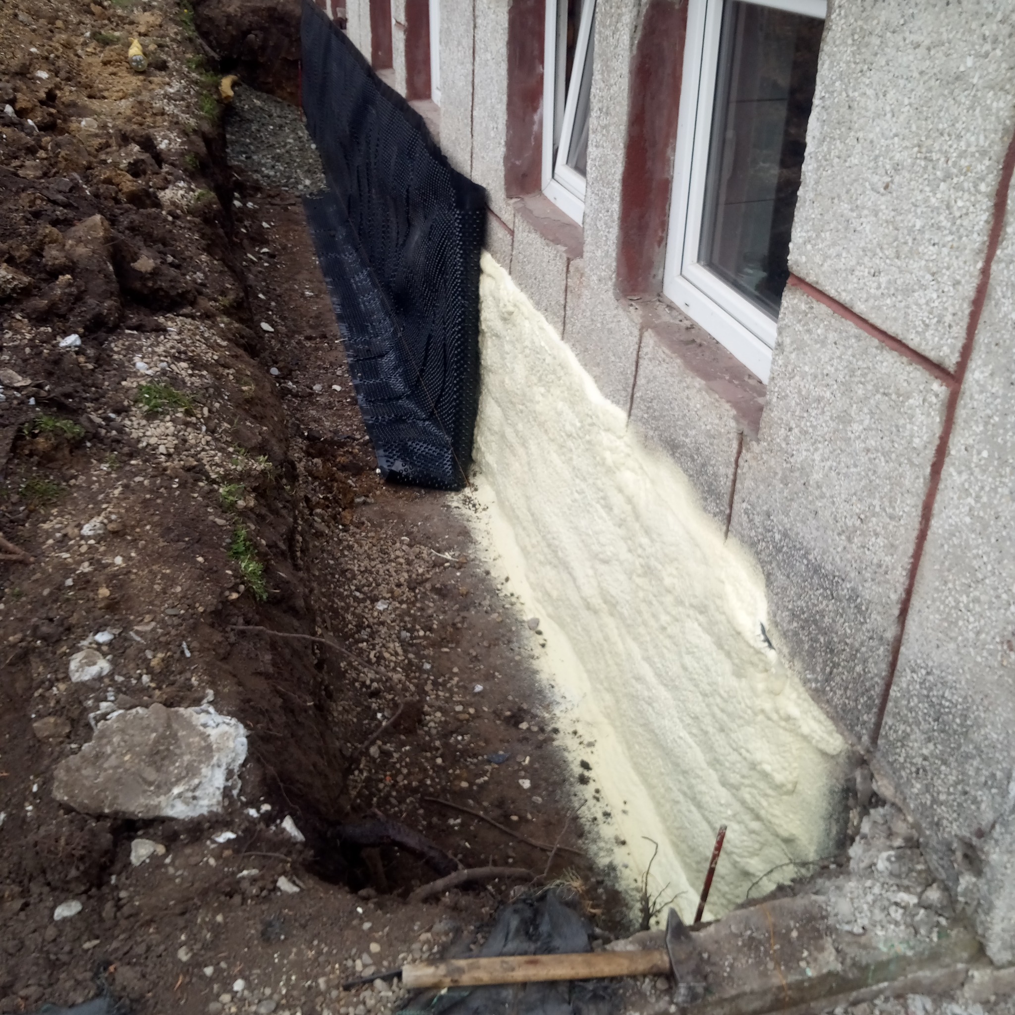 Fundament budynku w trakcie prac: widoczna czarna folia kubełkowa, warstwa izolacyjnej piany poliuretanowej oraz wykop z ziemią.