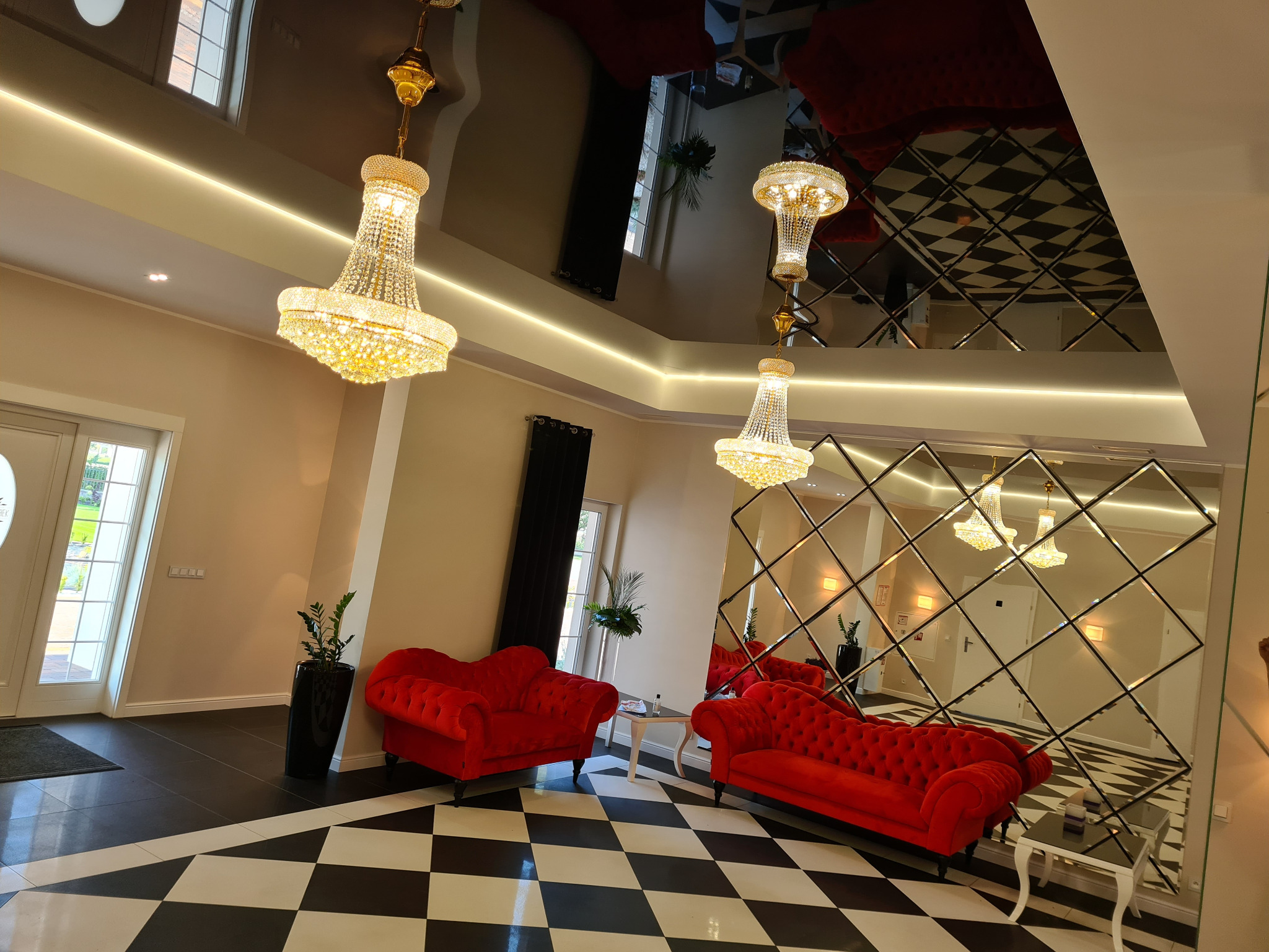 Eleganckie wnętrze z błyszczącą czarno-białą podłogą w szachownicę, czerwonymi sofami typu Chesterfield, kryształowymi żyrandolami i lustrzaną ścianą w romby.