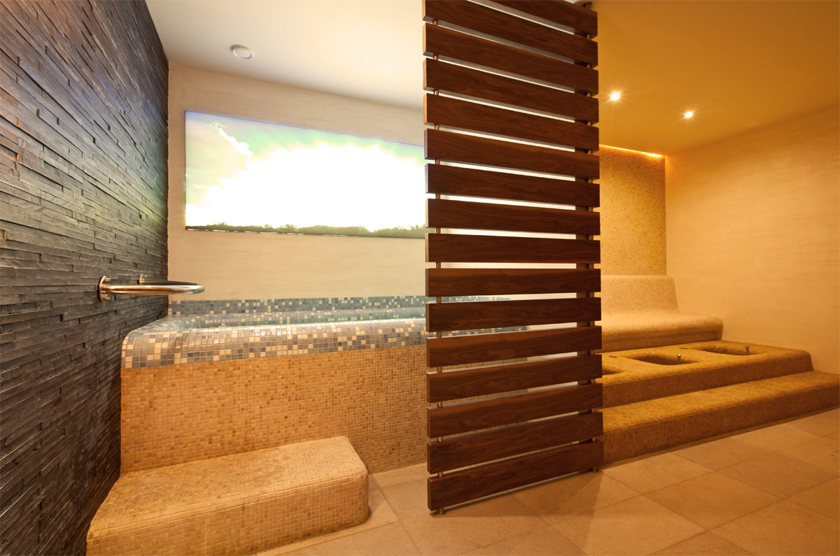 Nowoczesna łazienka z wyłożonymi mozaiką ścianami, drewnianą ażurową ścianką działową i podświetlanym oknem z widokiem na krajobraz.