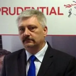 Portret mężczyzny w garniturze i niebieskim krawacie na tle logo firmy Prudential.