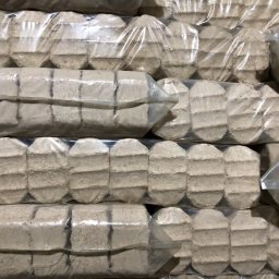 Pietrucha Gerard Zakład Stolarski - Ułożone w stos pakiety z drzewnym brykietem w przezroczystej folii, widoczne charakterystyczne żłobienia na powierzchni brykietu.