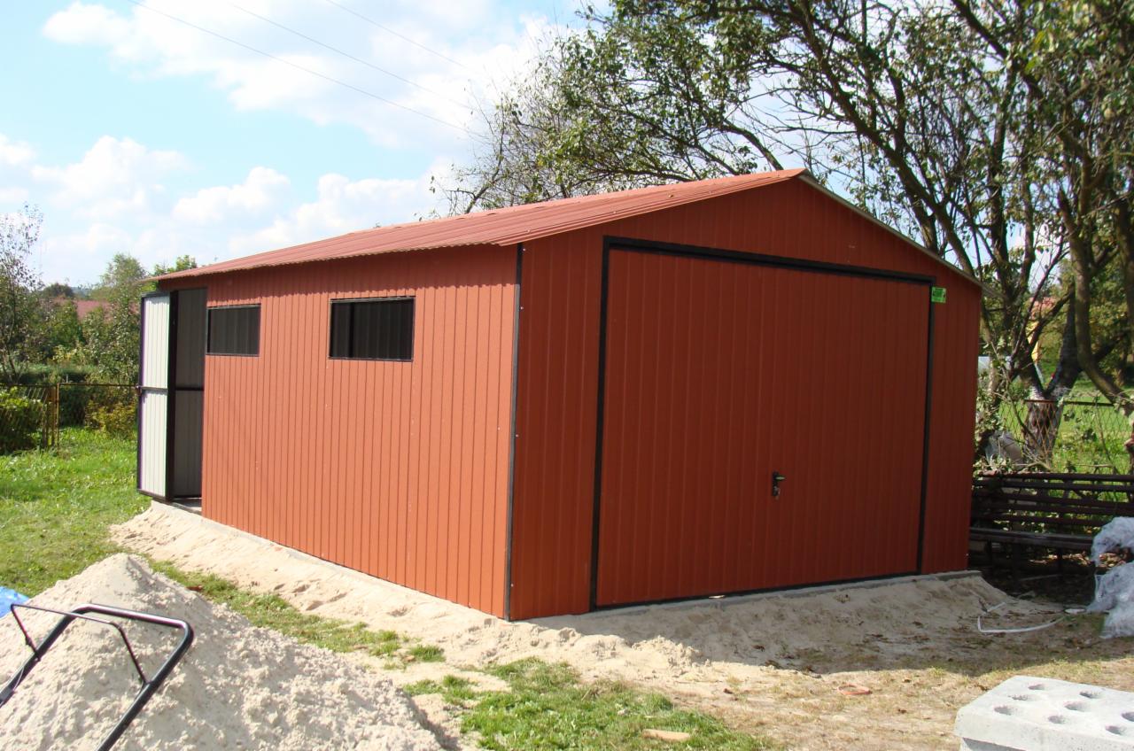 Pomarańczowy garaż blaszany z dwoma oknami i otwartymi drzwiami bocznymi, widoczny na tle zieleni i błękitnego nieba.