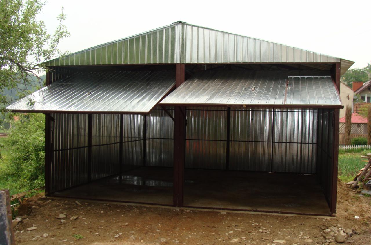 Dwu-stanowiskowy garaż blaszany z podnoszonymi drzwiami, konstrukcja z metalowych profili, widok z zewnątrz na nierówny teren.